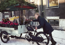 849829 Afbeelding van een bloemenverkoper die zijn brombakfiets vooruit duwt.